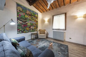 A living room with a sofa, a small table, a decorative wall hanging, a radiator, and a window with curtains. - San Giovanni House by Mmega (Florence)