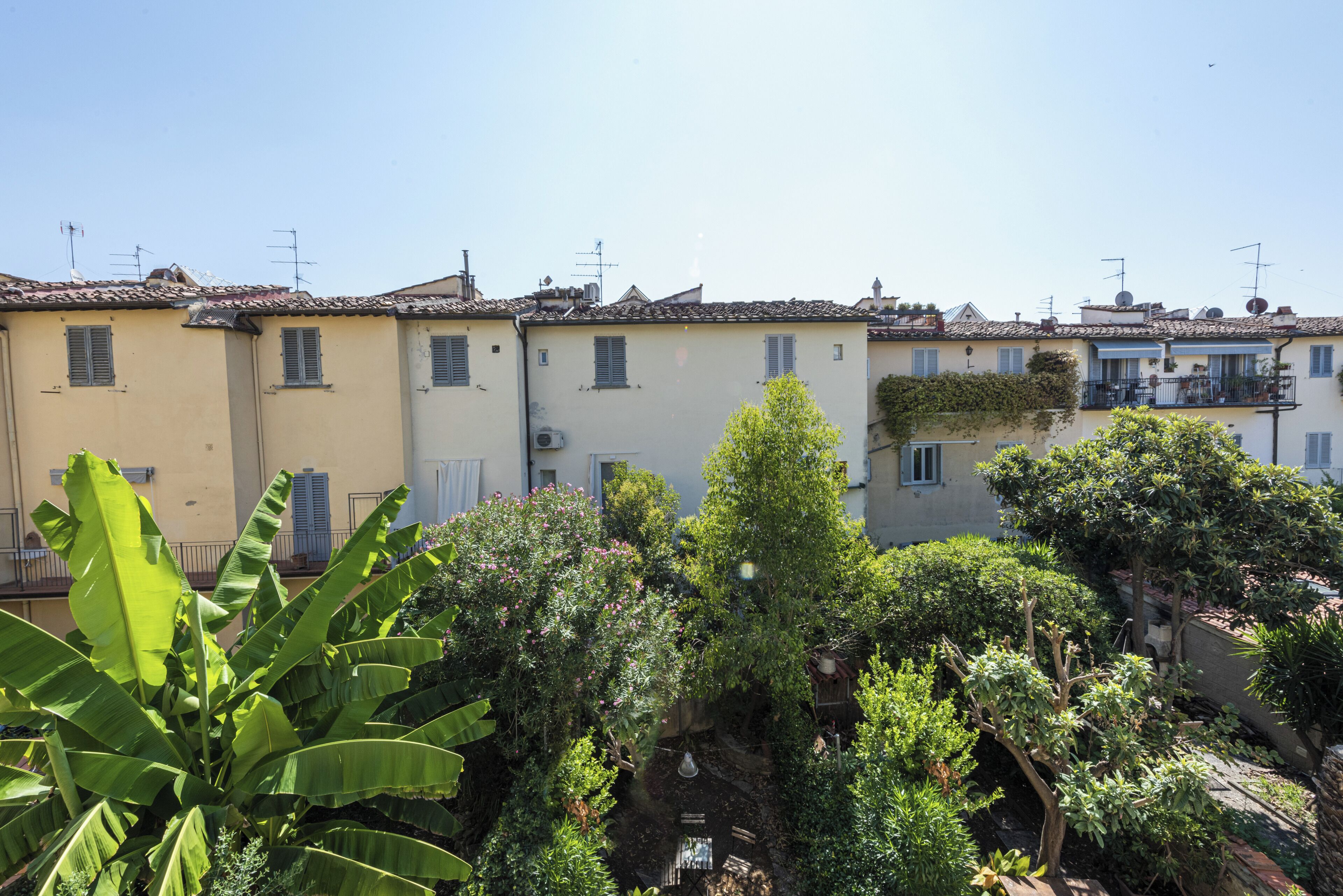 A row of terracotta-roofed buildings with balconies, surrounded by lush greenery and banana plants.