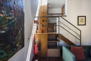 A staircase with wooden steps and metal railings, a fire extinguisher mounted on the wall, and a framed picture on the wall. - San Giovanni House by Mmega (Florence)