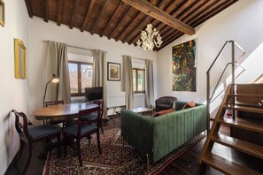 A living room with a wooden ceiling, a green sofa, a dining table with chairs, a television, and a staircase. - San Giovanni House by Mmega (Florence)