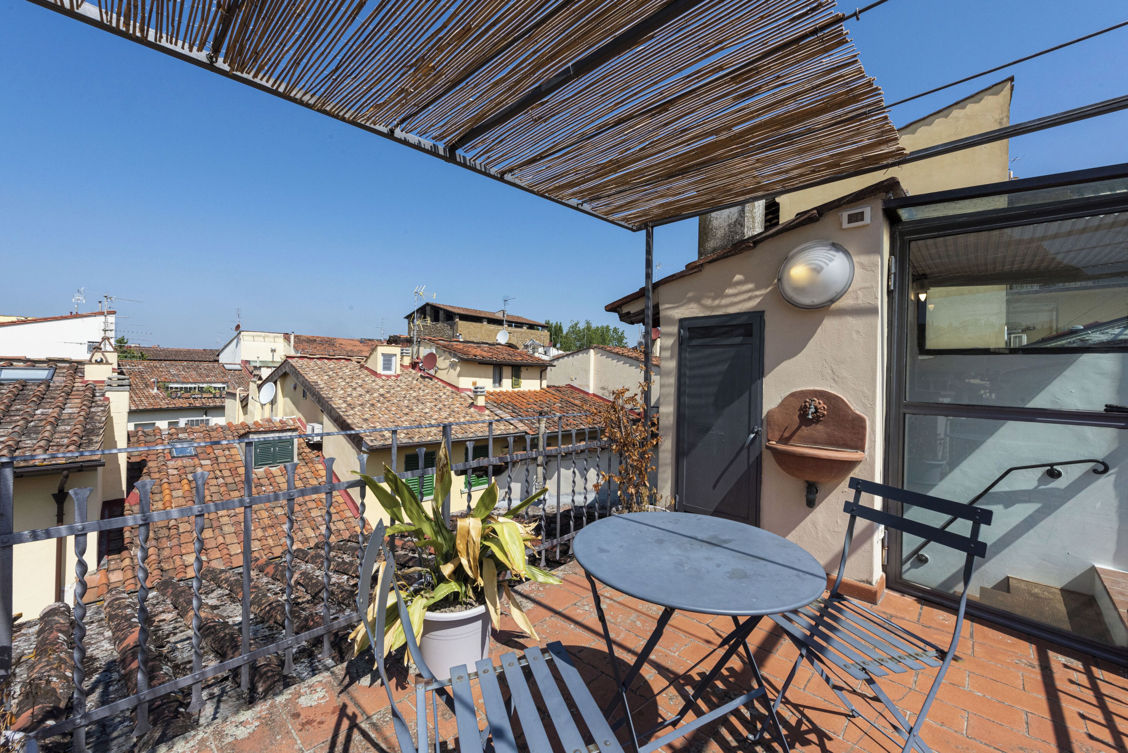A balcony with a table and chairs, a potted plant, and a view of neighboring buildings.