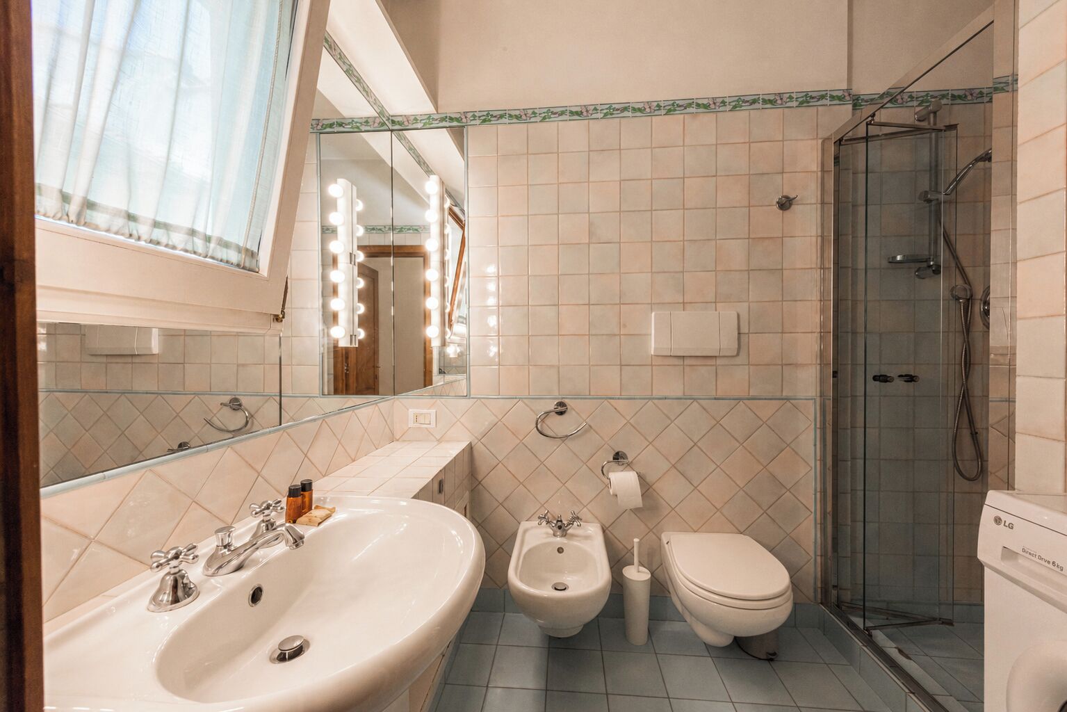 A bathroom with a large mirror, vanity with a sink, bidet, toilet, and a glass-enclosed shower area.
