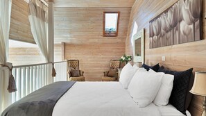A bedroom with a large bed, two chairs, a window, and a mirror on the wall.