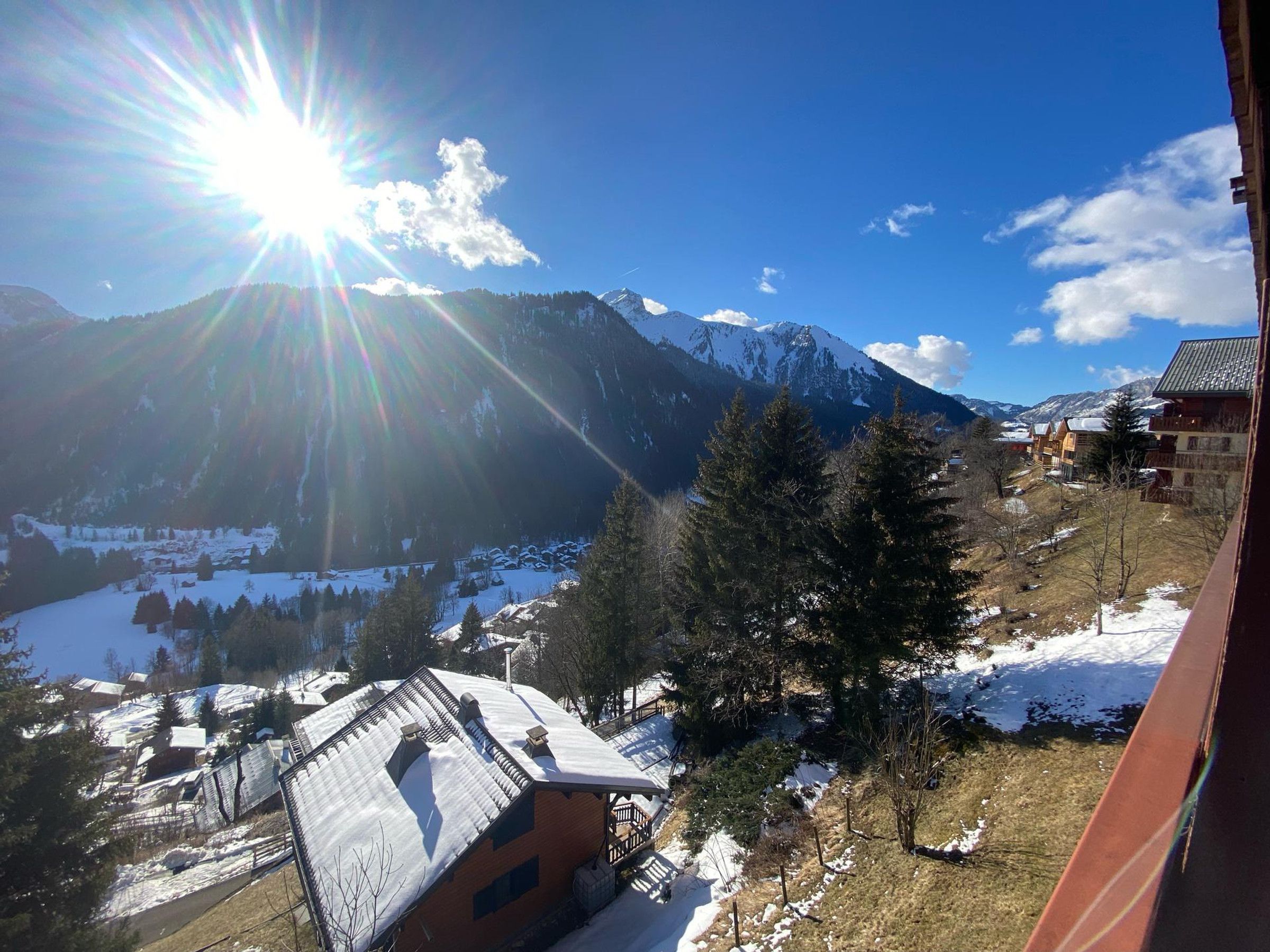 A mountain village with snow-covered roofs and houses, a clear sky, and a sun shining brightly.