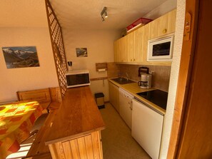 A compact kitchen with a wooden table, a microwave, a coffee maker, and a dishwasher.