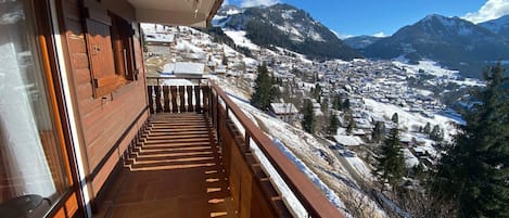 A wooden balcony with a view of a snow-covered village and mountains.