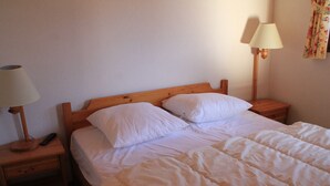 A neatly made bed with white linens, two bedside lamps, and a wooden nightstand with a remote control.