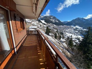 Un balcón de madera con vistas a un pueblo cubierto de nieve y montañas.
