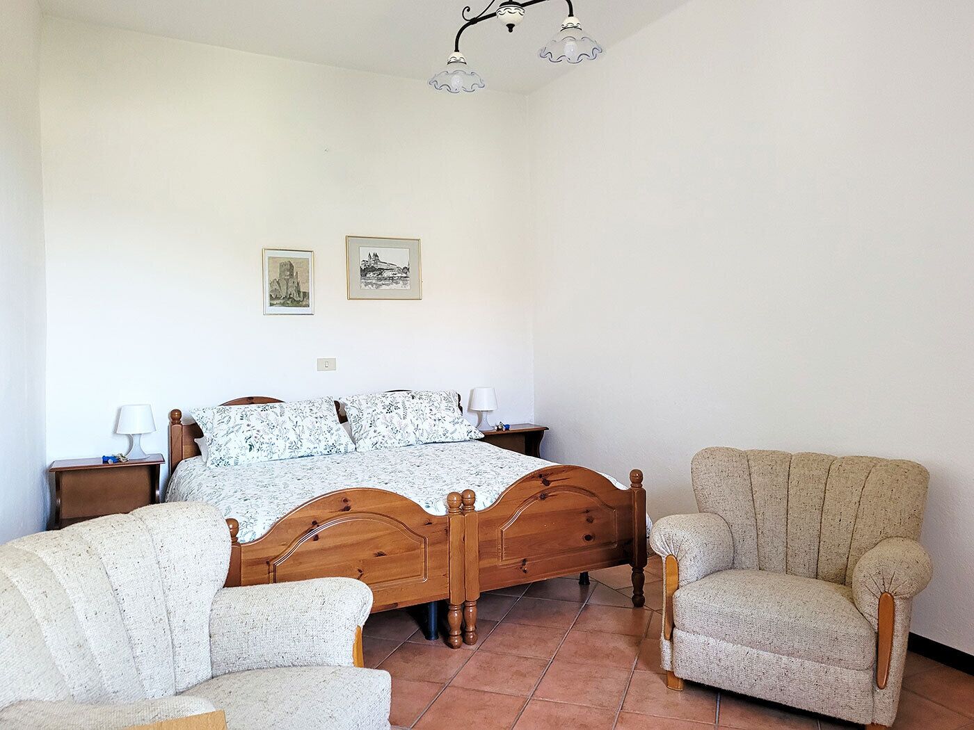 Ein Schlafzimmer mit einem hölzernen Bett, zwei Stühlen, einem Nachttisch, einer Lampe und zwei gerahmten Bildern an der Wand.