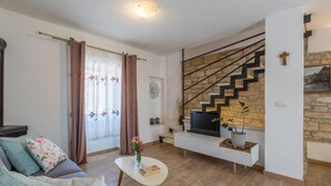 A living room with a sofa, a coffee table, a TV on a white stand, a staircase with a stone wall, and a window with curtains.