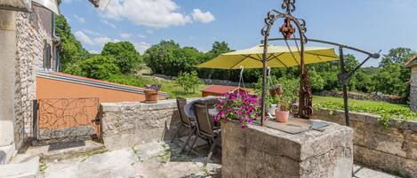 A stone patio with a table and chairs, a hanging chair, and a yellow umbrella.