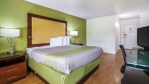 A hotel room with a bed, two bedside lamps, a desk with a chair, a television, and a door. - Econo Lodge Airport Near Billy Graham Parkway (Charlotte)