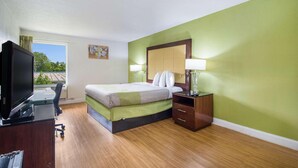 A hotel room with a bed, bedside table, lamp, desk with a computer, and a TV. - Econo Lodge Airport Near Billy Graham Parkway (Charlotte)