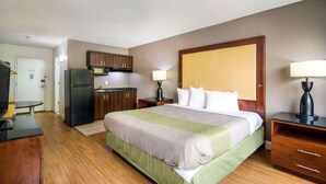 A hotel room with a bed, a desk, a refrigerator, a lamp, and a door. - Econo Lodge Airport Near Billy Graham Parkway (Charlotte)