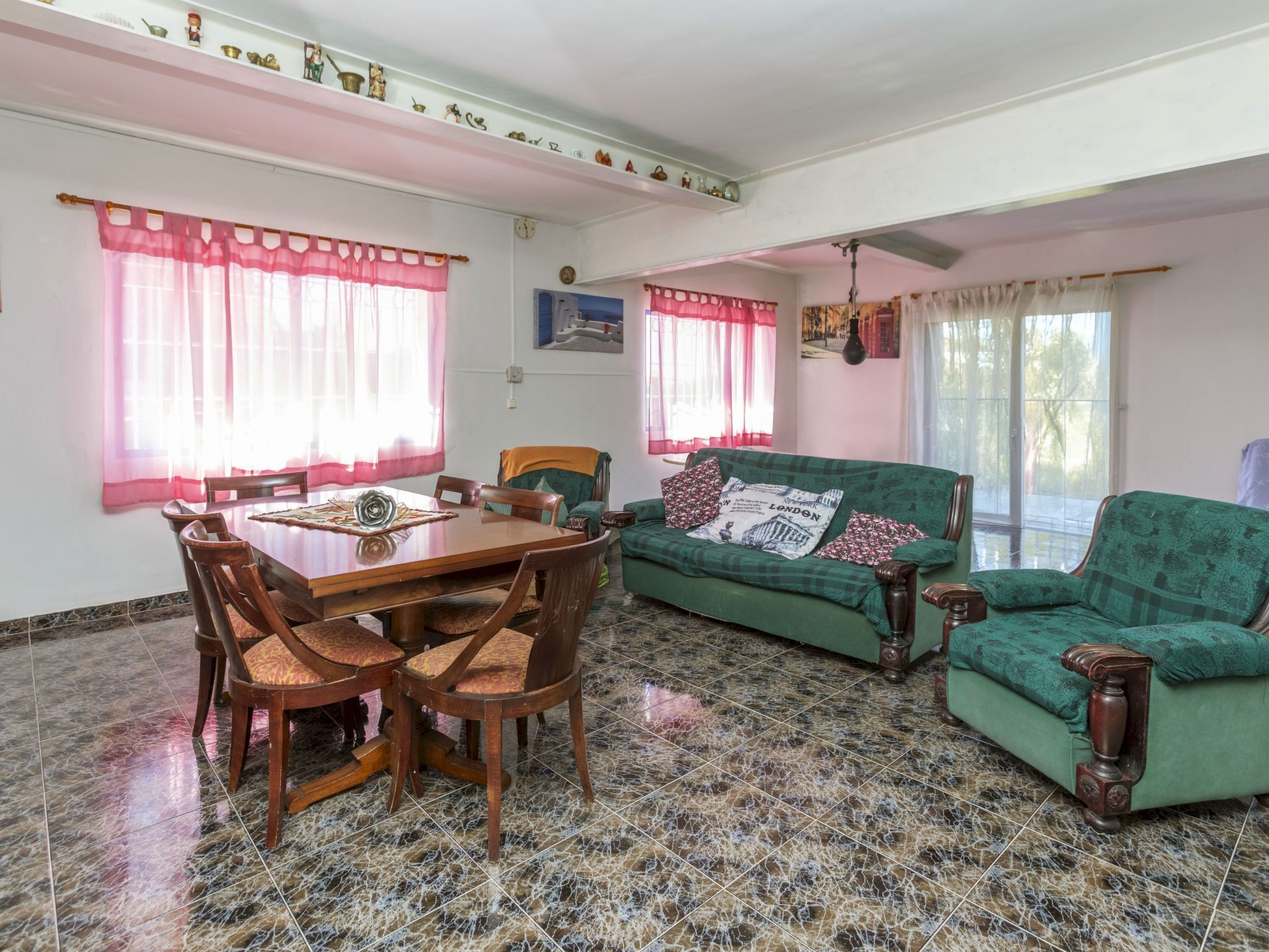 A dining area with a wooden table and chairs, a green sofa, and a tiled floor.