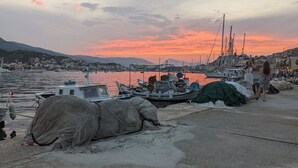 A harbor with boats docked, a waterfront promenade, and a backdrop of hills.