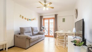 Un salon moderne avec un canapé gris, une table à manger avec des chaises, un ventilateur de plafond et un téléviseur.