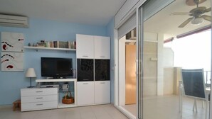 Un salon moderne doté d’un téléviseur à écran plat, de meubles blancs et d’une porte coulissante en verre donnant sur un balcon.