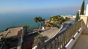 Un balcon donnant sur la mer, une route et un immeuble à la façade blanche.