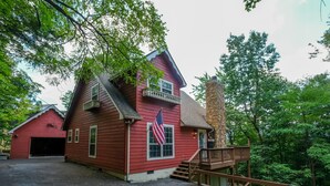 A red wooden building with a stone chimney, a wooden deck, and an American flag. - Cutest Wears Valley cottage that looks like it is straight out of a storybook! (Sevierville)