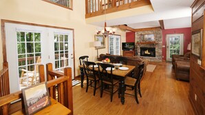 A dining area with a wooden table and chairs, a fireplace, and a television in the background. - Cutest Wears Valley cottage that looks like it is straight out of a storybook! (Sevierville)