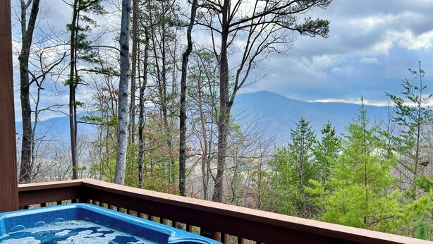 A hot tub on a wooden deck with a view of a forest and mountains. - Cutest Wears Valley cottage that looks like it is straight out of a storybook! (Sevierville)
