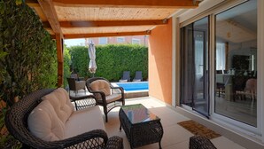 Eine Terrasse im Freien mit Korbmöbeln, einem Glastisch und Blick auf einen Swimmingpool.