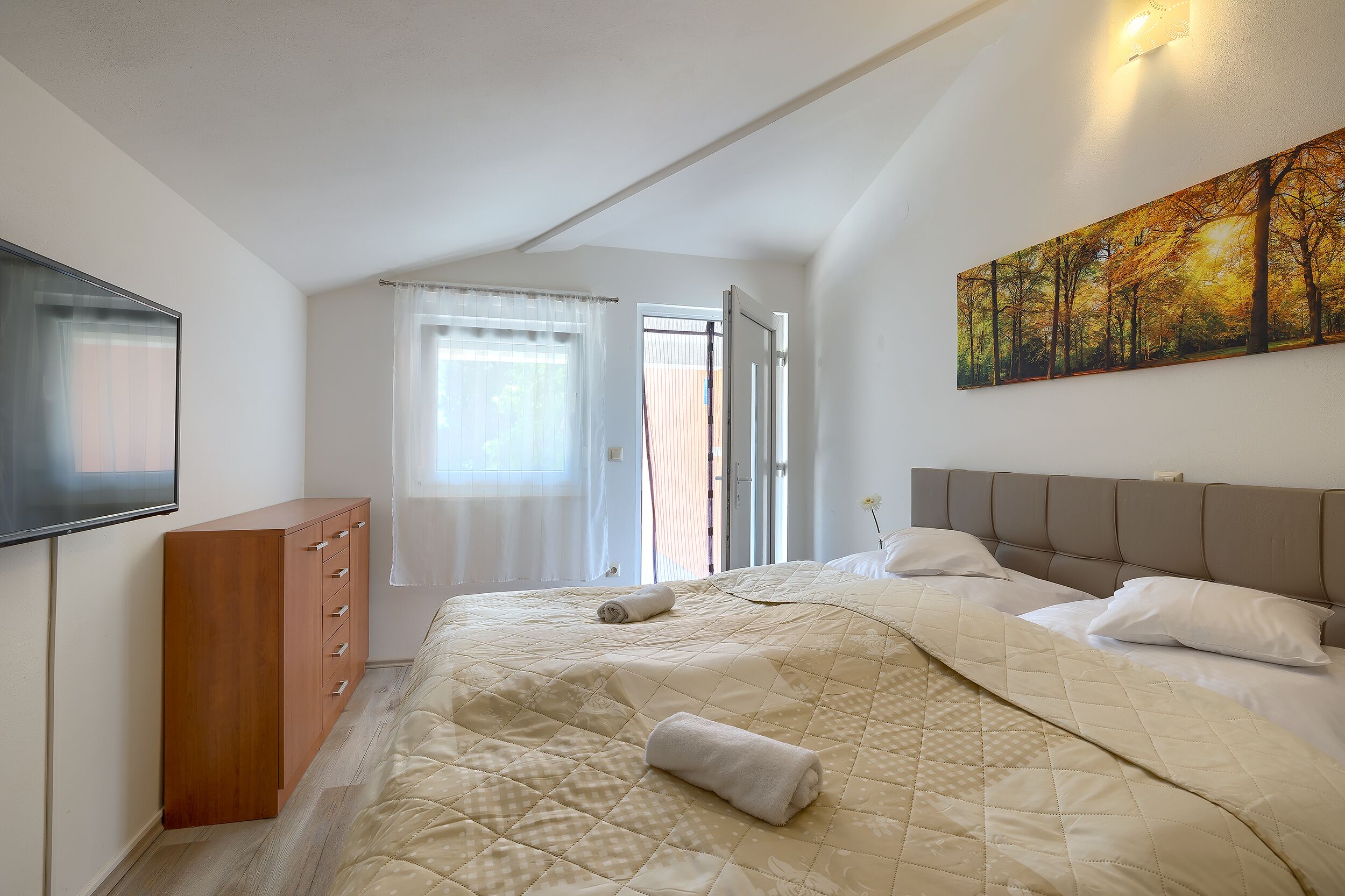 A bedroom with a bed, a dresser, a painting, and a window.