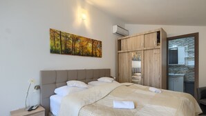 Ein ordentlich bezogenes Bett mit einer Tagesdecke, ein Nachttisch mit einer Lampe und ein Baumgemälde an der Wand.