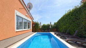 Ein rechteckiger Swimmingpool mit klarem, blauen Wasser, umgeben von einer beigen Fliesenveranda.