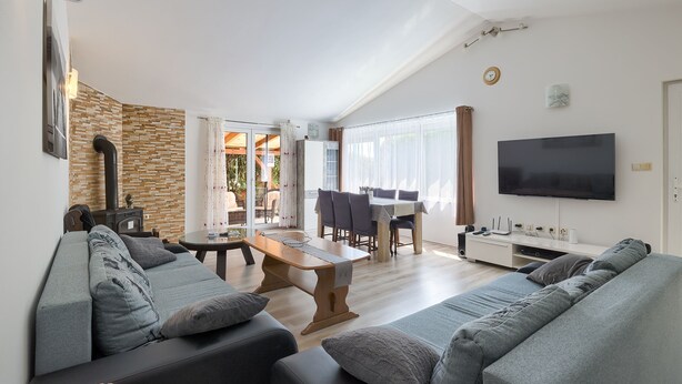 Ein modernes Wohnzimmer mit einer Couch, einem Couchtisch und einem Fernseher. Im Hintergrund ist ein Essbereich mit Tisch und Stühlen zu sehen.