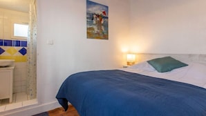 Un dormitorio con cama, un cuadro de una playa, una mesita de noche con lámpara y un baño con cortina de ducha.