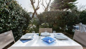 Un área de comedor al aire libre con una mesa preparada para cuatro personas, rodeada de follaje y árboles.