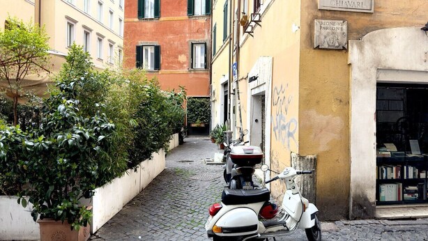 A narrow cobblestone street with a parked scooter, buildings with signage, and a narrow alleyway. - Charm and Style by Campo de' Fiori (Roma)