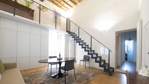 A spacious living area with a dining table, chairs, a patterned rug, a staircase, and a view into the kitchen. - Charm and Style by Campo de' Fiori (Roma)
