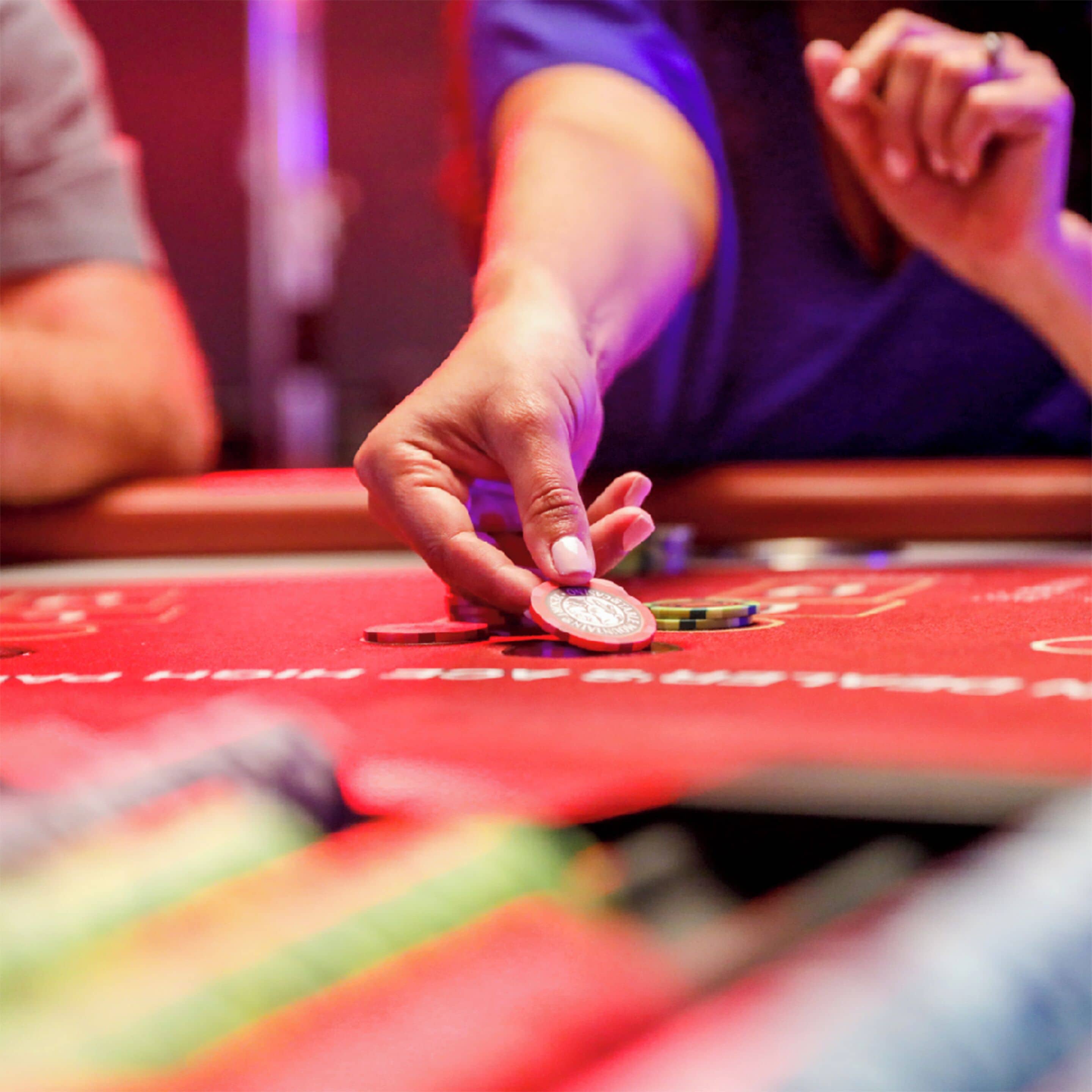 A hand placing a chip on a red table with visible text, likely in a casino setting.