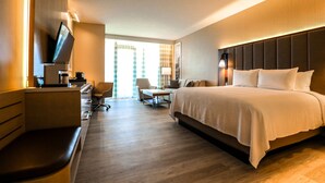 Hotellihuone, jossa on suuri sänky, työpöytä tuolilla, televisio ja ikkuna, jossa on verhot.