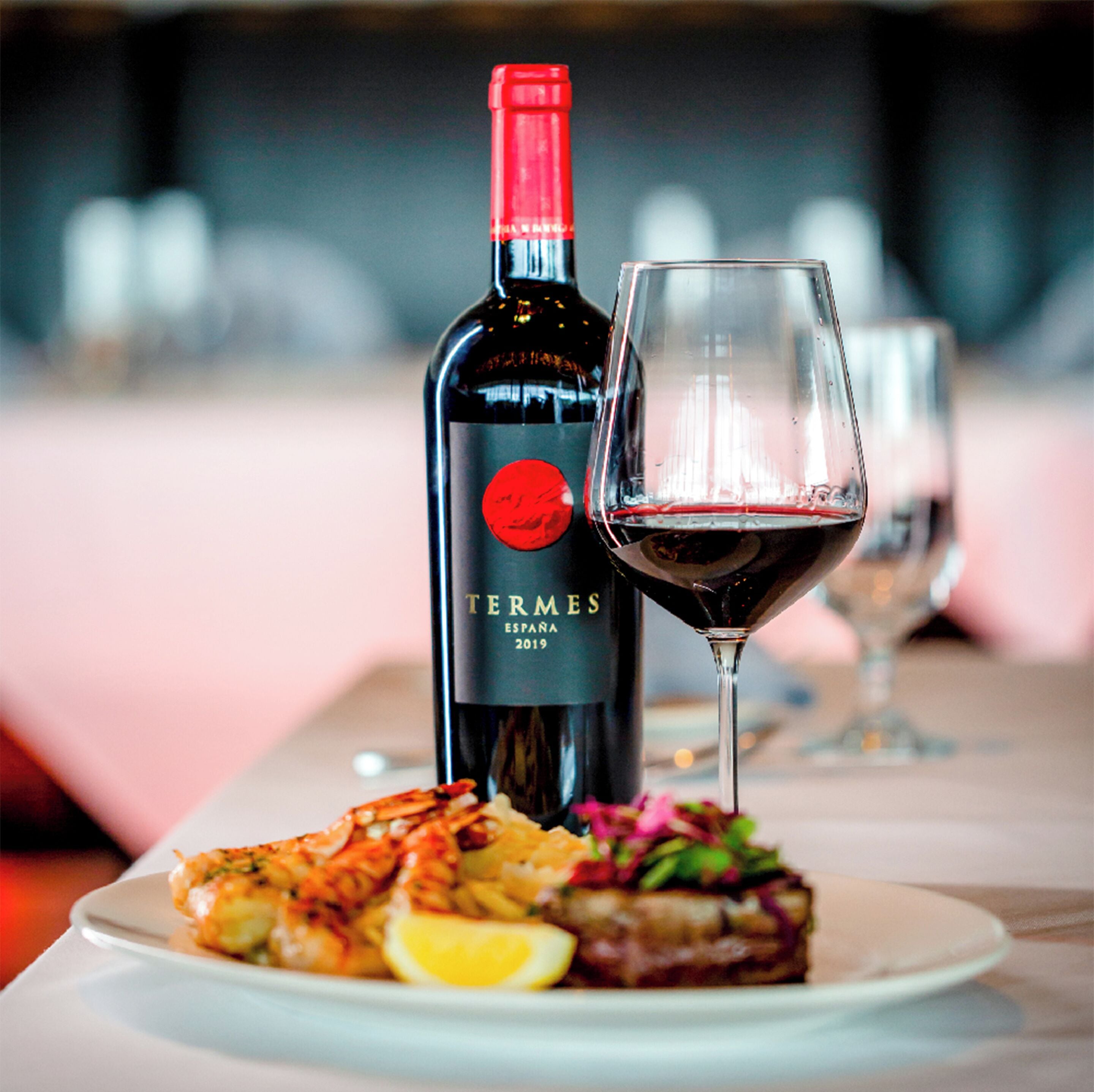 A bottle of wine, a glass of red wine, and a plate of food on a table.