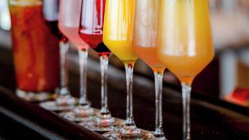 A row of colorful cocktails in glasses with garnishes, displayed on a bar counter.