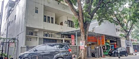 A multi-story building with a concrete facade, a parked car, and a tree in front.