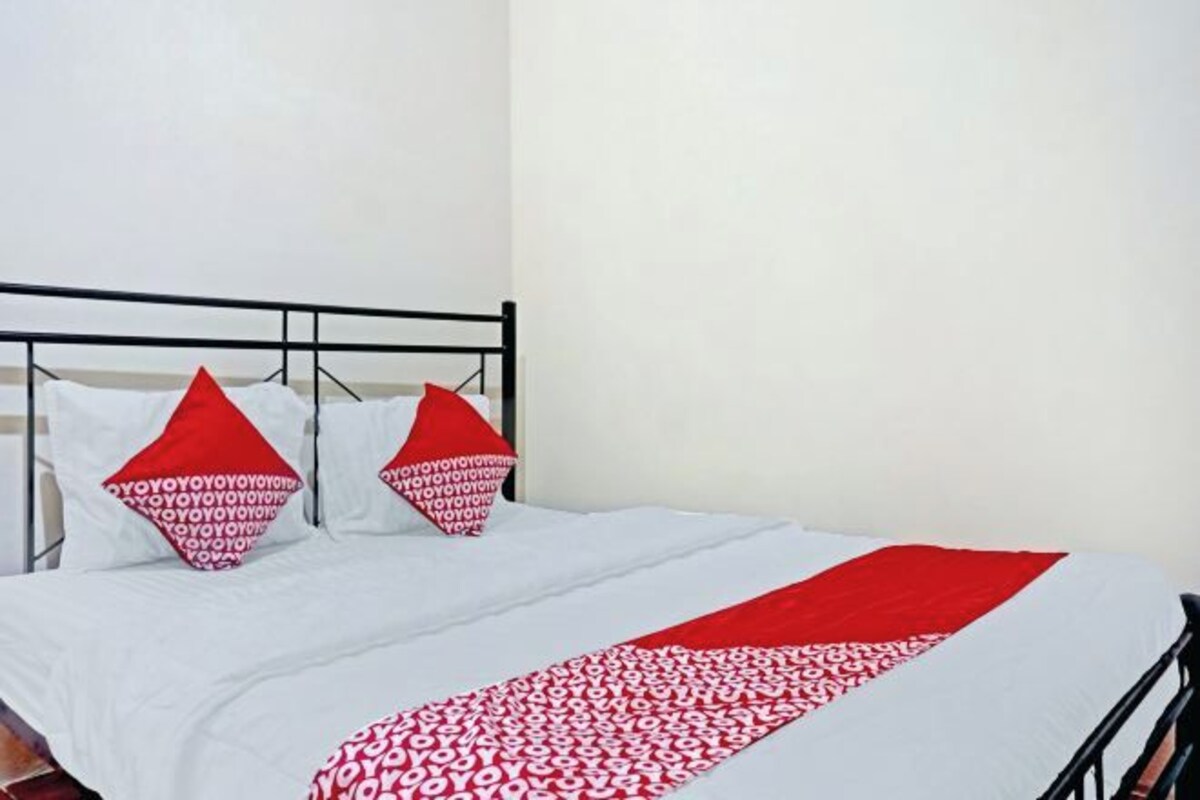 A bed with a white and red bedspread, two red pillows, and a black metal headboard.