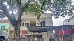 A two-story building with a gated entrance, a covered area in front, and a tree providing shade.
