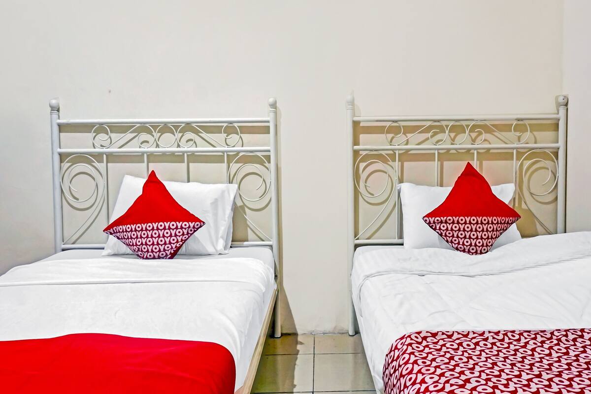 Dos camas individuales con estructuras metálicas blancas y almohadas rojas y blancas con estampado.