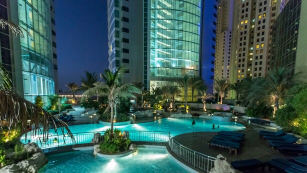 A nighttime pool area with clear water, palm trees, and lounge chairs. - Al Fattan - Sea View - Luxury JBR - Free Beach Resorts Access! (Dubai)
