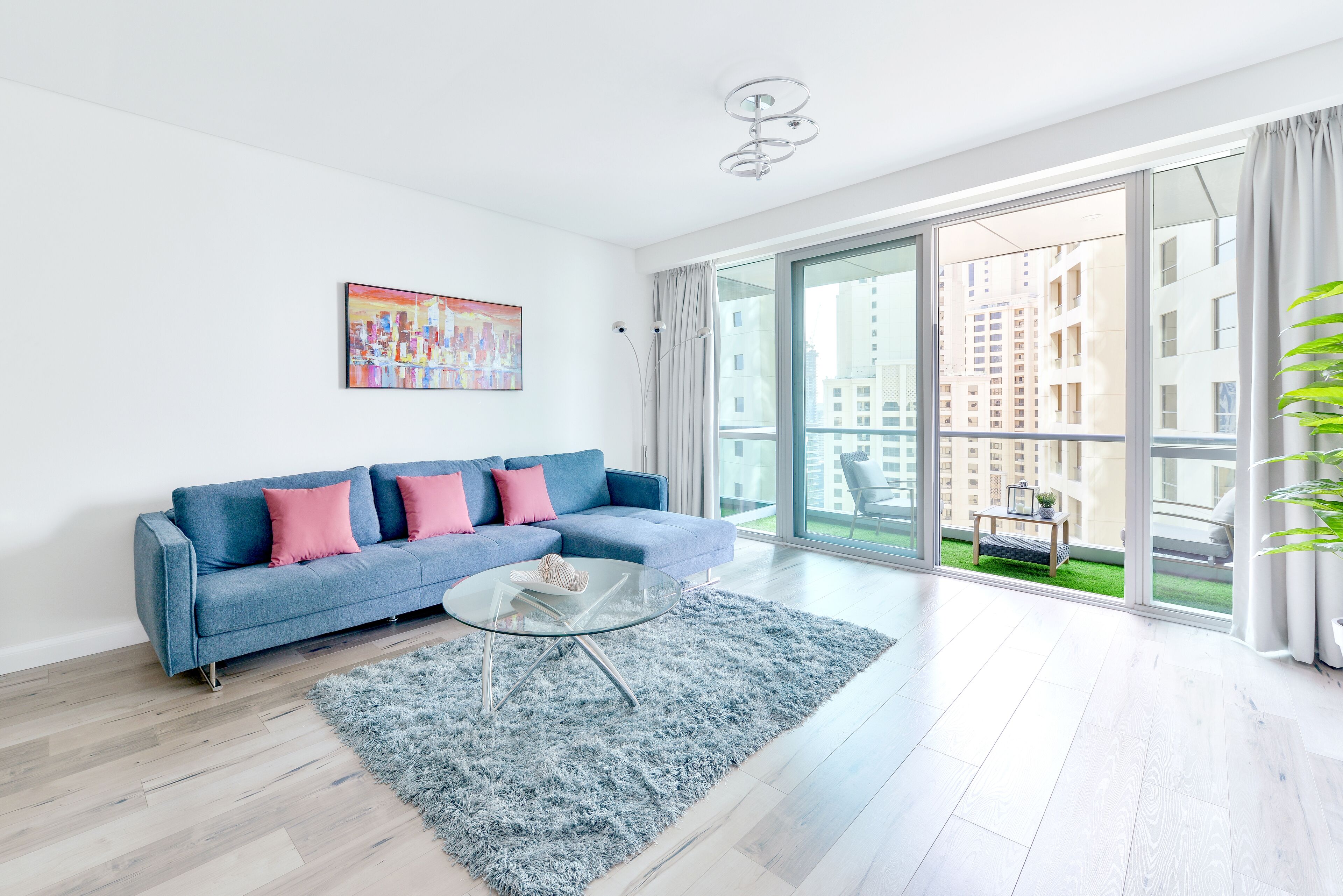 A modern living room with a blue sofa, a glass coffee table, and a large window offering a view of a cityscape.