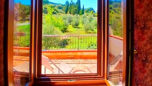 Ein Zimmer mit einem großen Fenster, das einen Blick auf eine grüne Landschaft mit Bäumen und bewölktem Himmel bietet.