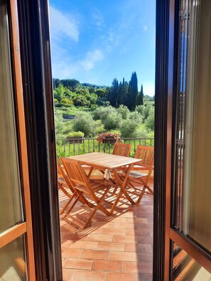 An open patio with a wooden table and chairs, a view of a lush garden, and a clear sky. - Charming apartment, complete and comfortable with terrace and panoramic view! (Ghirlanda)