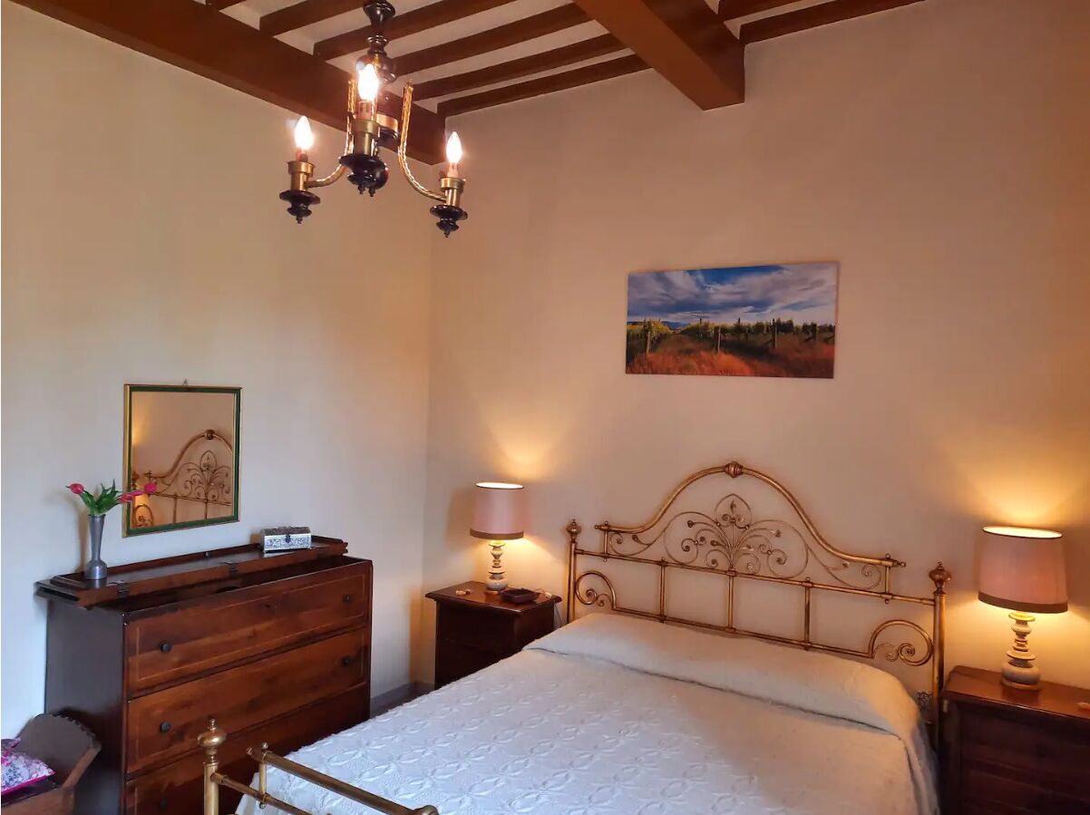 Ein Schlafzimmer mit einem hölzernen Bett, einer Kristallleuchter, Nachttischlampen, einer Kommode und einem gerahmten Bild an der Wand.