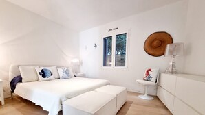 Ein modernes Schlafzimmer mit einem großen Bett, einem kleinen Nachttisch, einem Sessel und einem Fenster mit Blick auf Bäume.