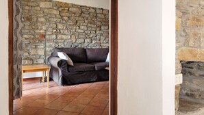 Un salon avec un mur en pierre, un canapé foncé, une table d’appoint en bois et un sol carrelé.